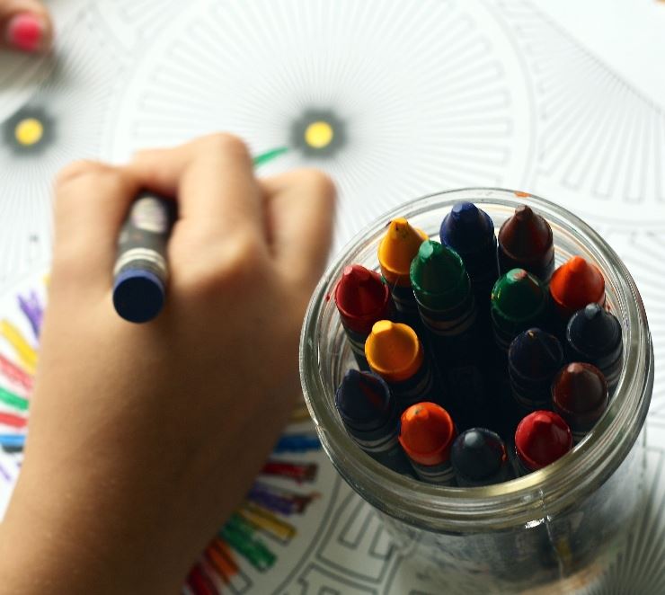 Shows a child's hand using crayons to create a picture