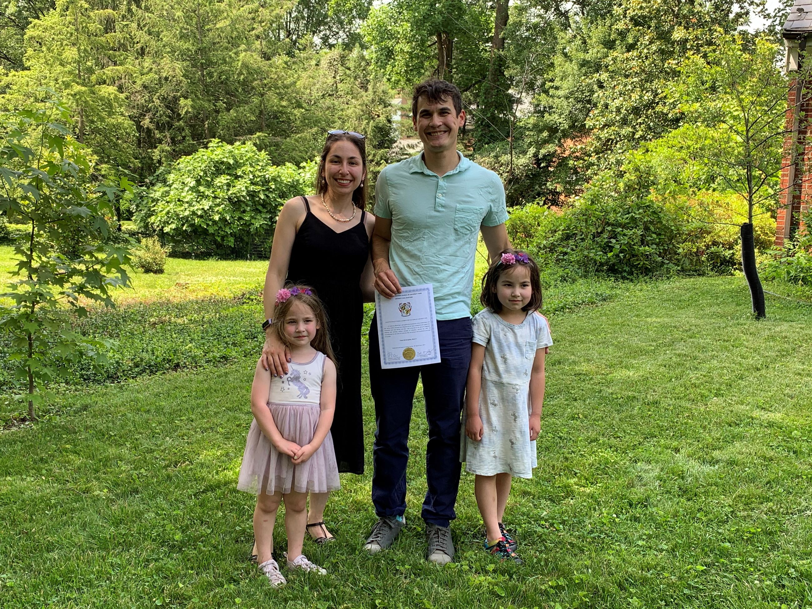 CM McGaughey posing with his wife and two daughters in the yard of their home.